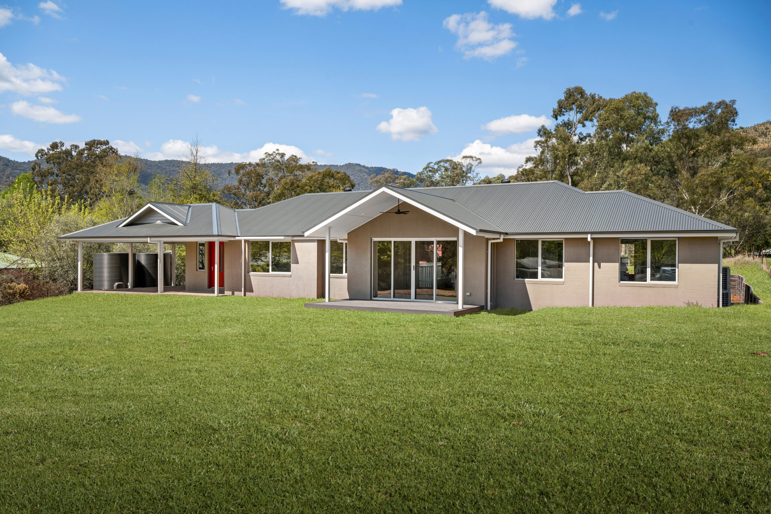 Light grey house with a dark grey roof, green grass and blue sky.